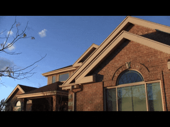 Red brick house with triangular rooflines and large windows under a clear blue sky with a leafless tree branch.