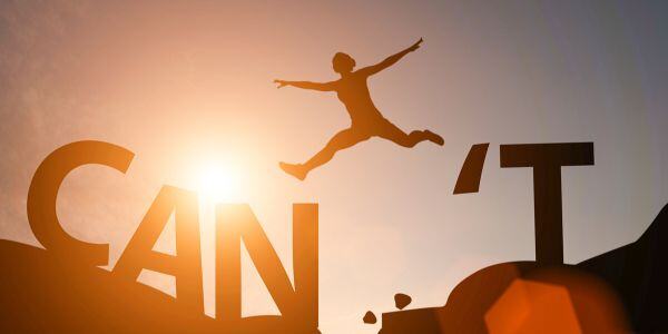 Silhouette of a person leaping over the gap between 'CAN' and 'T' with sunlight in the background.