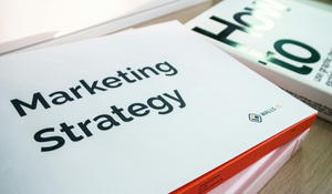 A book titled Marketing Strategy lying on a wooden table next to another book partially visible.