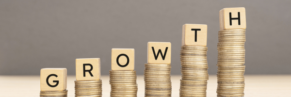 Wooden blocks spelling GROWTH atop increasing stacks of gold coins on a neutral background.
