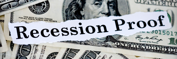 Torn paper with Recession Proof text overlaid on scattered US hundred dollar bills background.
