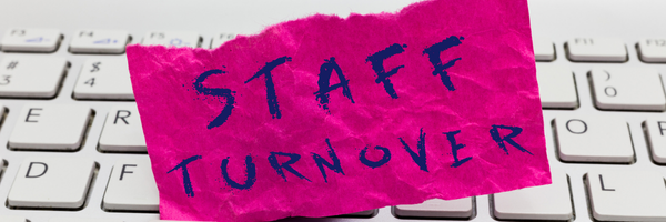 Crumpled pink paper with STAFF TURNOVER text placed on a white computer keyboard symbolizing employee turnover.