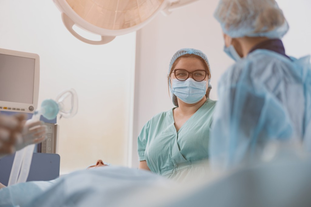 Nurse assisting doctors during surgery in operation room of clinic