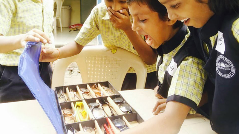 Kids in India smile after opening a box of new eyeglasses.