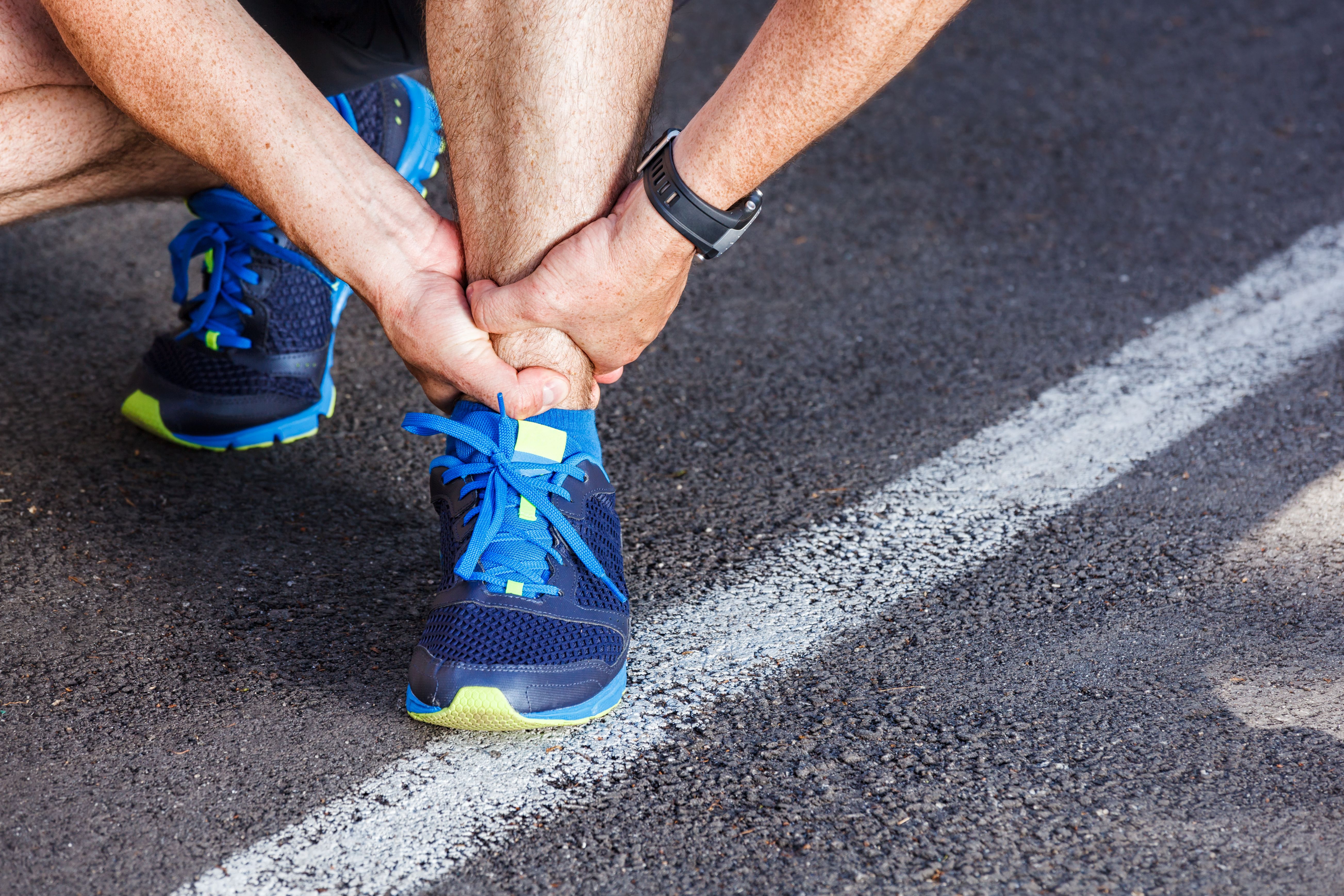 Close up on man's feet in athletic shoes as he grasps ankle in pain