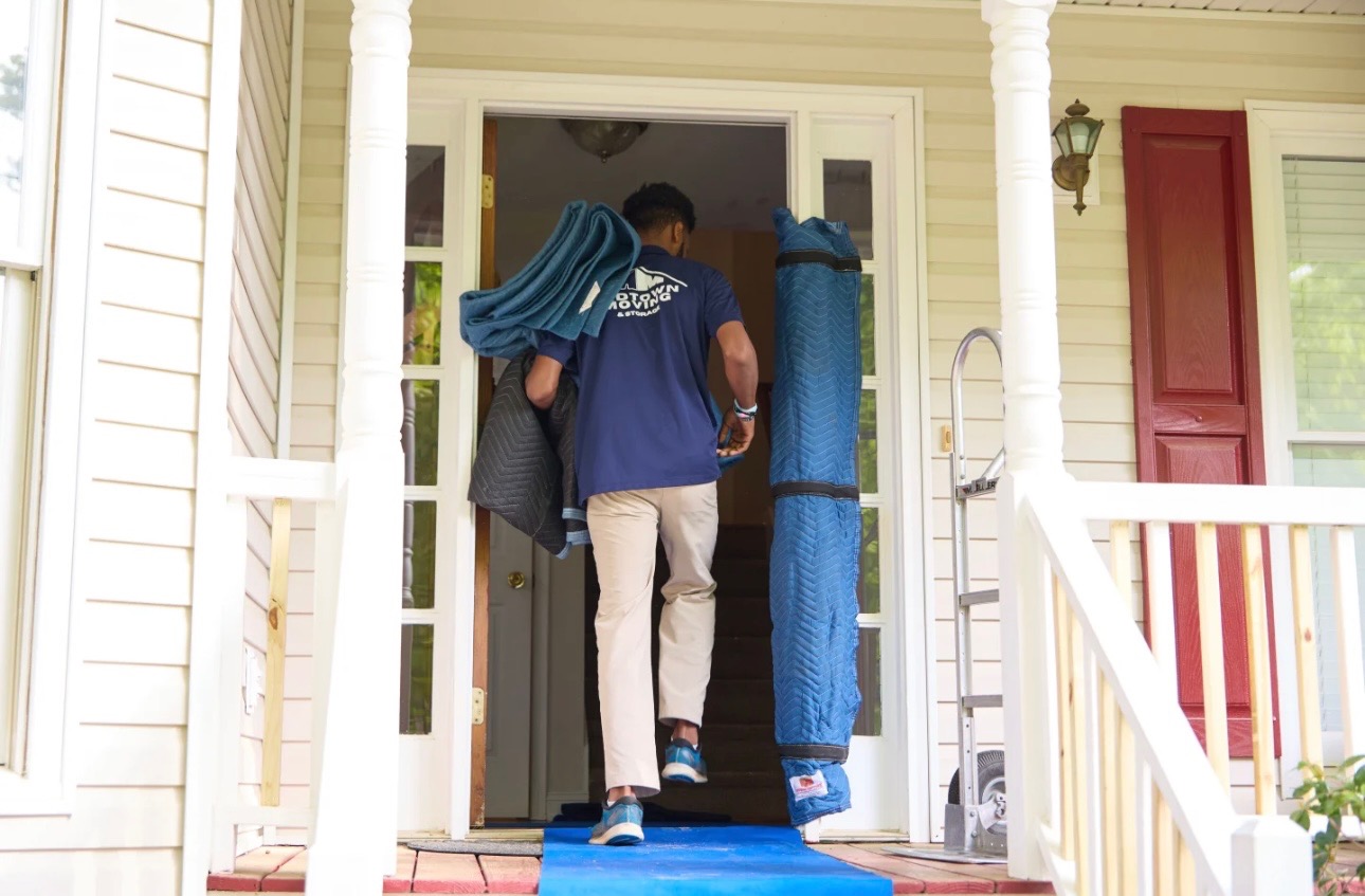 Midtown mover carrying moving blankets and a rolled floor runner through a front door