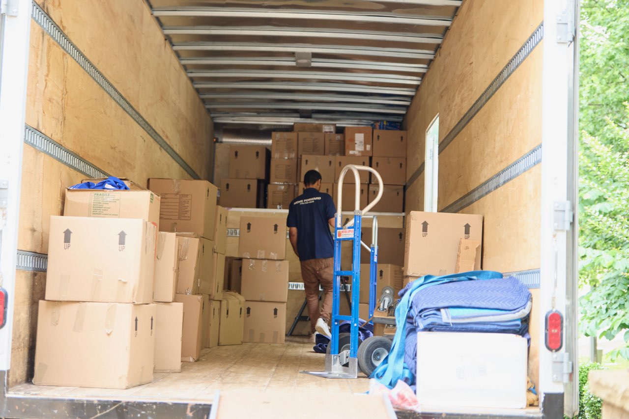 Midtown mover loading packed boxes into the truck, with a hand truck and moving blankets at the door