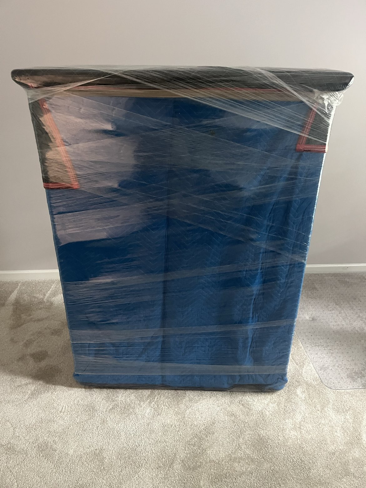 A dresser wrapped in a blue moving blanket and shrink wrap