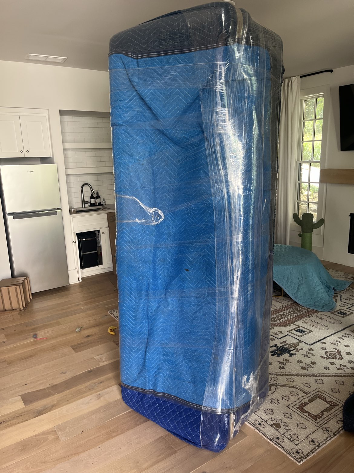 A sofa wrapped in a moving blanket and shrink wrap, standing in a living room before the move