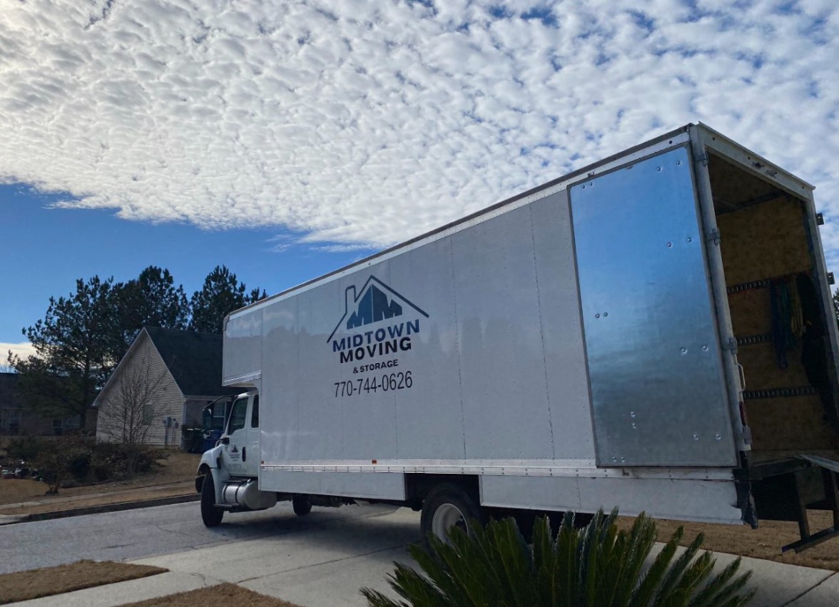 Midtown Moving box truck parked in a driveway, with local moving, long distance, packing and unpacking, and junk removal listed on its side