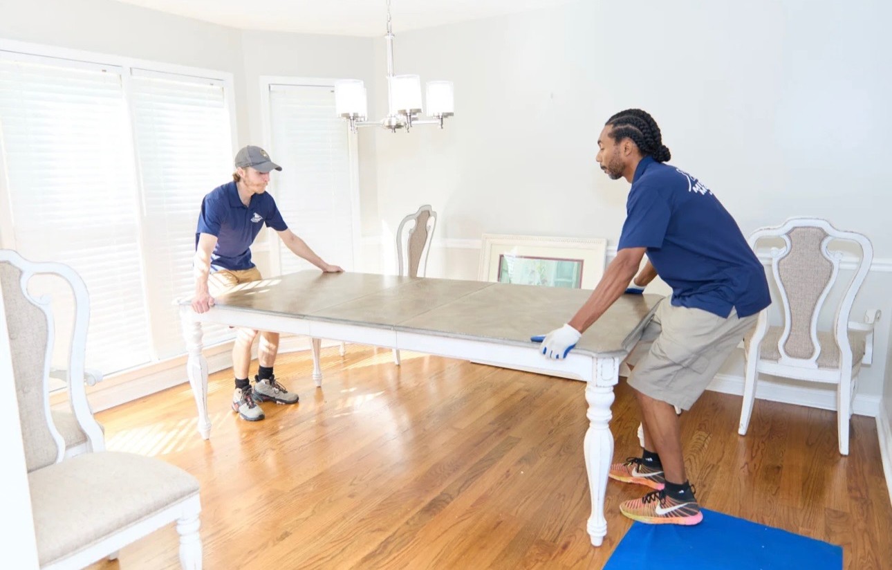 Two Midtown movers carrying a dining table through a home
