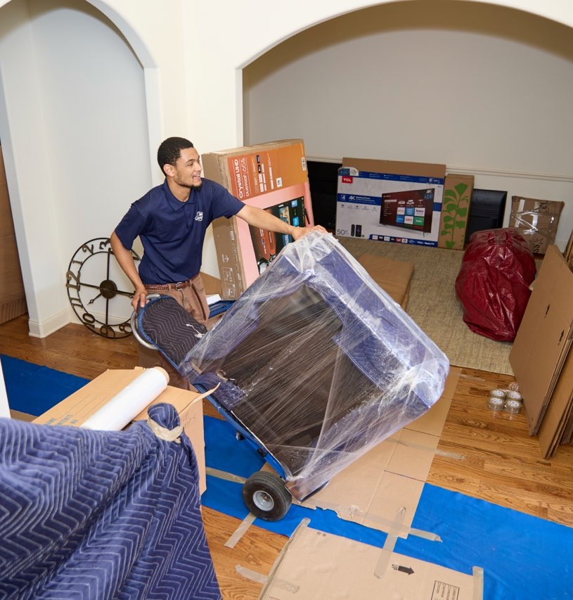 Midtown mover wheeling a shrink-wrapped piece on a dolly over a covered floor