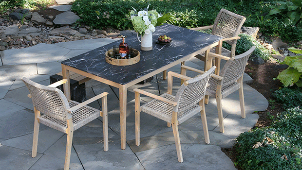 Outdoor patio setup with wooden frame table, black stone top, and four wicker chairs on stone flooring.