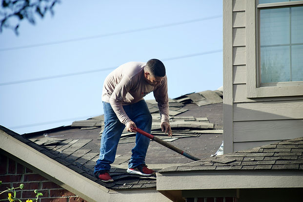 Man dressed casually, removing shingles from a house roof