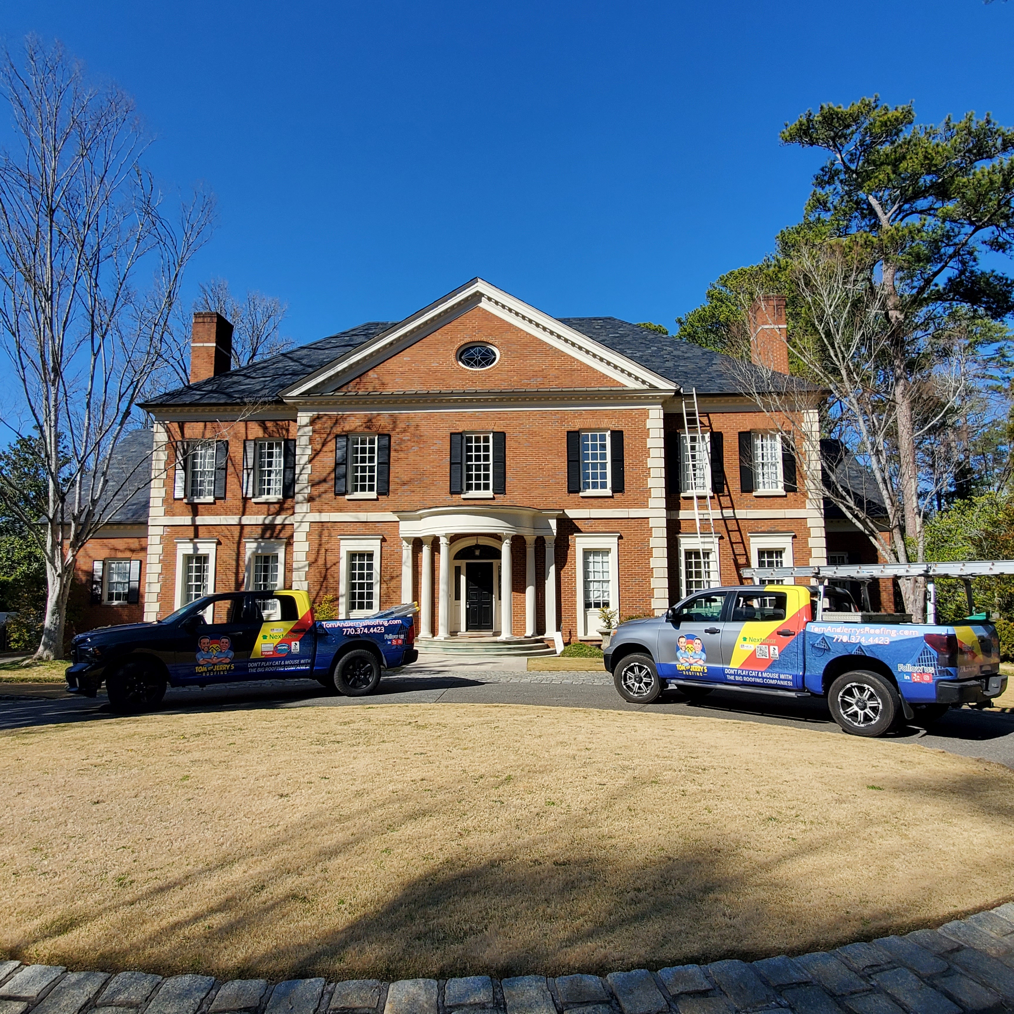 Two Tom and Jerry's Roofing work trucks parked in front of a beautiful home with a newly completed roof, highlighting expert craftsmanship and quality service.